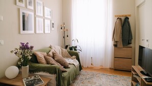 Ein Wohnzimmer mit einem grünen Sofa, einem Couchtisch mit Blumenvase, einem Fernseher und einem Holzkasten.