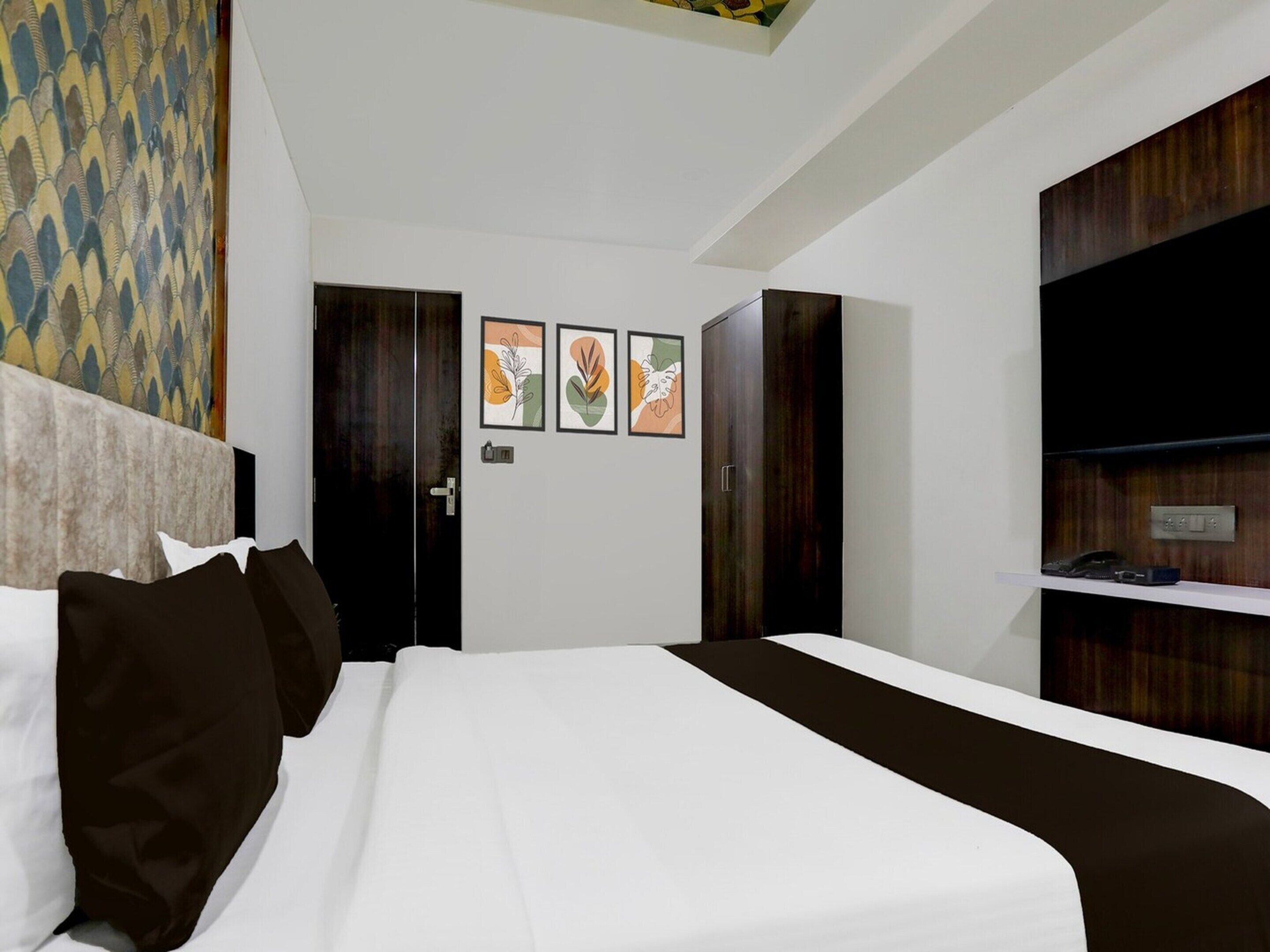 Une chambre d’hôtel moderne avec un grand lit, une armoire en bois foncé et un petit bureau avec un téléphone.