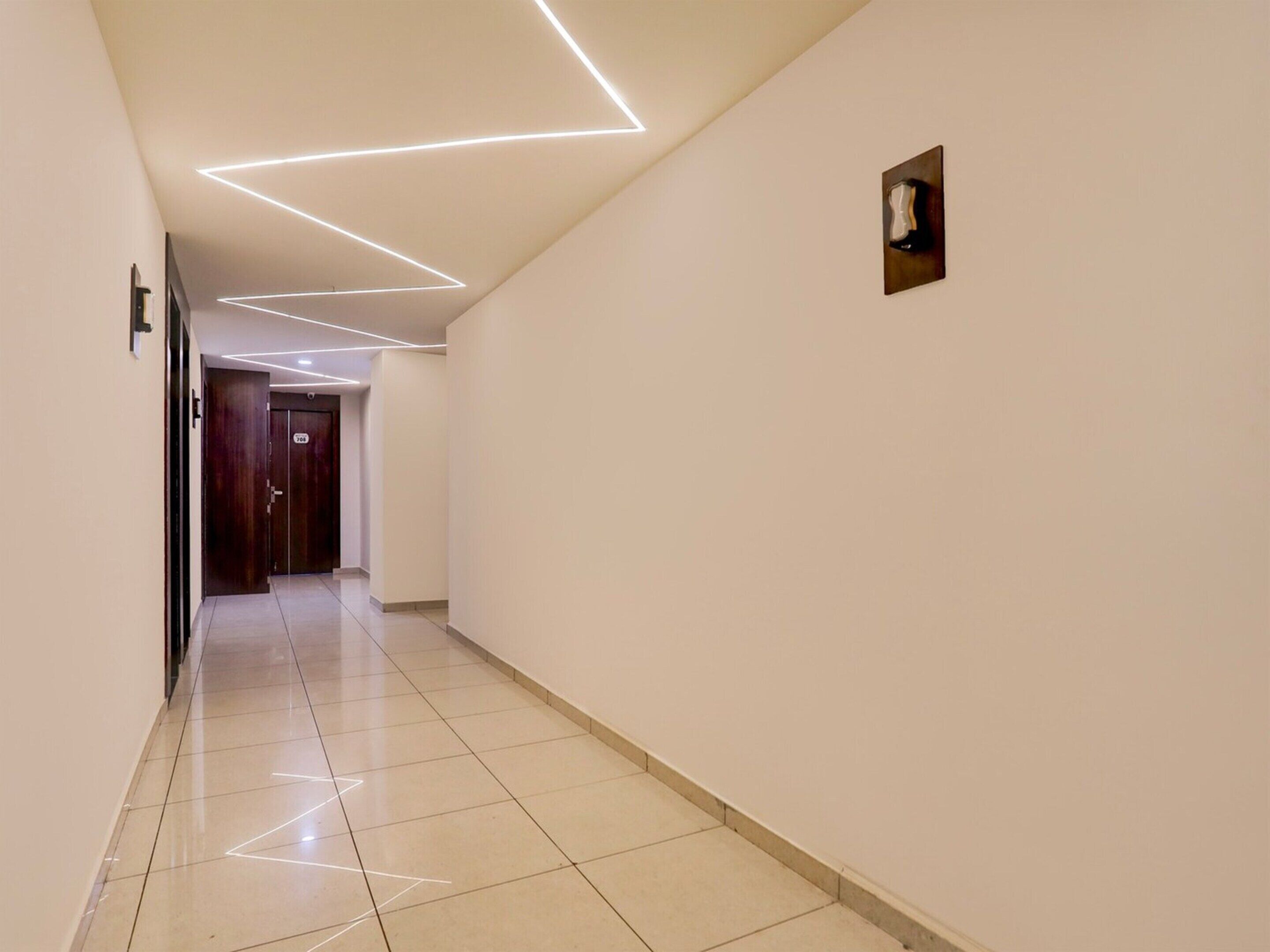 A corridor with a modern ceiling design, a door with a number, and a small wall-mounted light fixture.