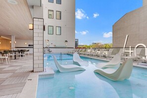 A modern outdoor pool area with lounge chairs and a building with large windows. - Boutique Studio with Pool, Gym & Walk to Midtown (Nashville)