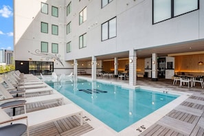 A rooftop pool with lounge chairs, a bar area, and a modern building with large windows. - Boutique Studio with Pool, Gym & Walk to Midtown (Nashville)