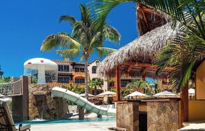 A resort with a water slide, palm trees, and a pool area. - Hacienda del Mar Oceanfront Resort: Beautiful 1 Bedroom Luxury Villa Suite (Cabo San Lucas)