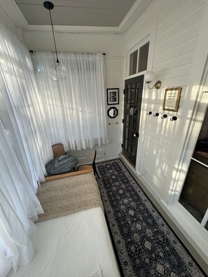 A room with a bed, a chair, a door with a mirror, a rug, and a light fixture. - Quintessential Cape May (Cape May)