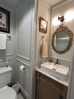 A bathroom with a toilet, a sink with a marble countertop, a mirror with an ornate frame, and a towel rack. - Quintessential Cape May (Cape May)