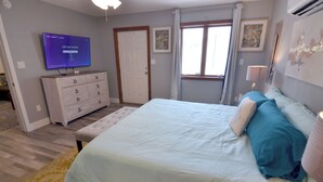 Une chambre à coucher comprenant un lit, une commode, un téléviseur affichant un écran de sélection de langues, une fenêtre avec des rideaux et un climatiseur fixé au mur.