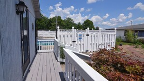 Une terrasse en bois avec une clôture blanche, une piscine et un ciel dégagé.
