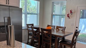 Una cocina con encimeras de granito, sillas de madera, una mesa de comedor, un refrigerador y una araña.