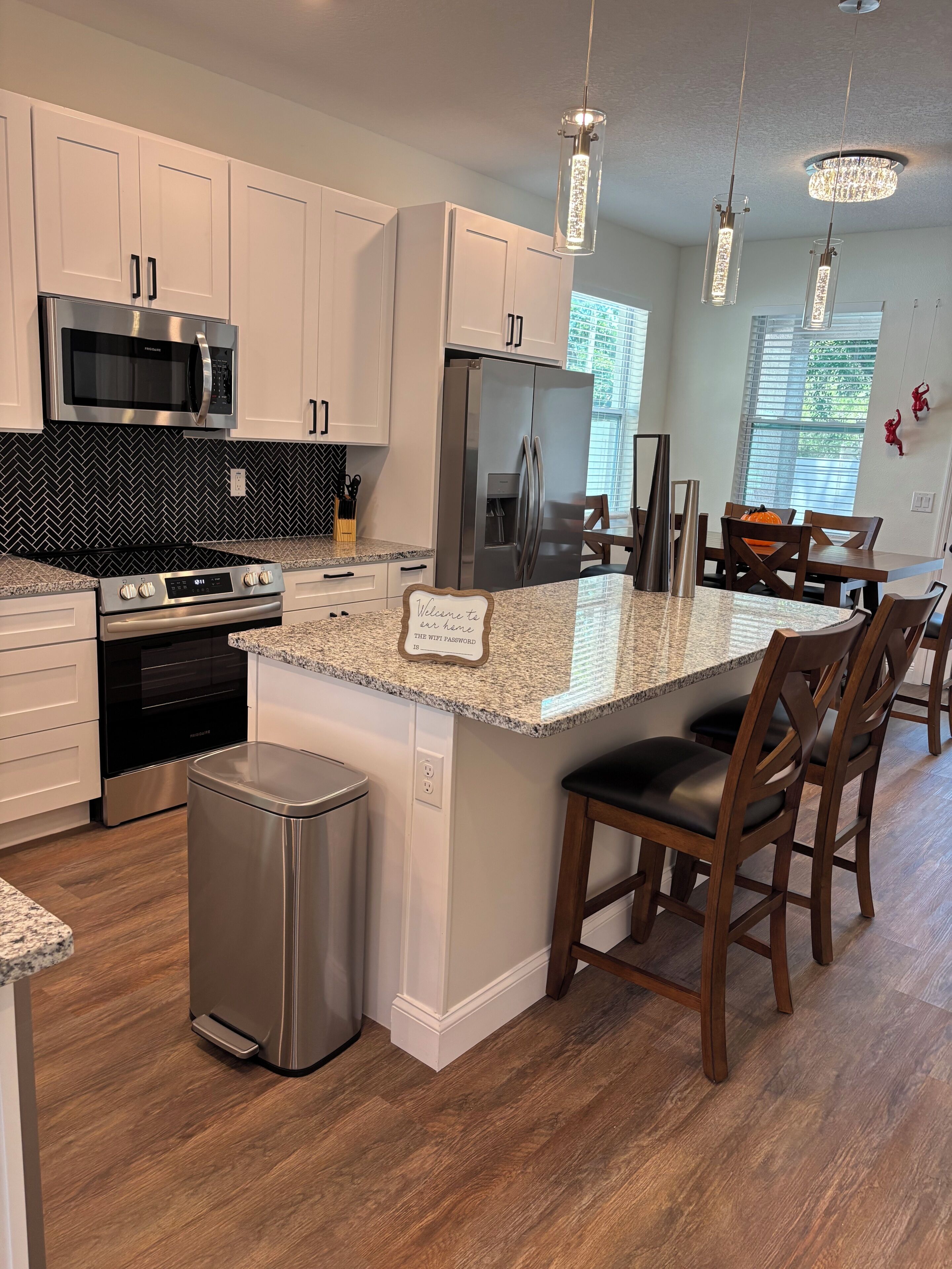 A modern kitchen with white cabinets, stainless steel appliances, a granite countertop, and a central island with bar stools.
