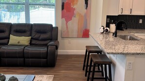 Una sala de estar moderna con un sofá de cuero, una mesa de centro y una zona de cocina con encimera de granito y taburetes de bar.