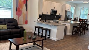 Una cocina moderna con armarios blancos, una isla central y un comedor con sillas de madera.