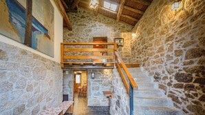A stone-walled interior with a wooden staircase, a bench, and a painting on the wall. - Casa das Xacias (A Airoá)