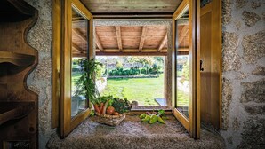 A rustic interior with a wooden ceiling, stone walls, and a view of a garden through an open doorway. - Casa das Xacias (A Airoá)