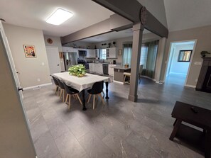 Une cuisine moderne dotée d’un îlot central, un coin repas avec une table et des chaises, et un couloir menant aux autres pièces.
