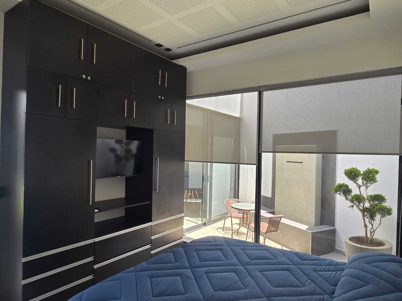 Quarto moderno com cama grande, roupeiro embutido e varanda com mesa e cadeiras.