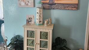 Paredes com quatro cenas de praia emolduradas, um armário com objetos decorativos e um vaso de planta.