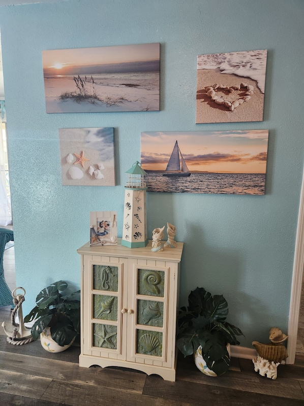 A wall with four framed beach scenes, a cabinet with decorative items, and a potted plant. - Surfside 2 blocks from Beach-Jetty-Splash pad 2 bdrm 3 bath (Freeport)