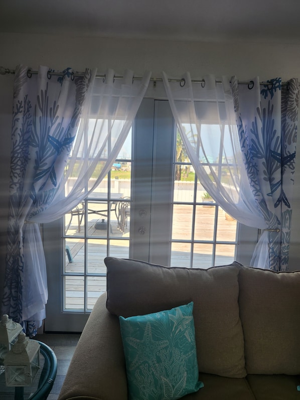 A room with a sofa, a table with a decorative item, and a view through a window with curtains.