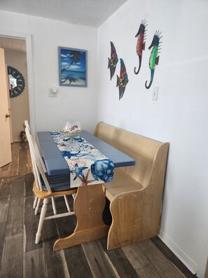 A dining area with a wooden bench, a table with a blue and white patterned tablecloth, and a painting of fish on the wall.