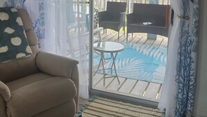 Quarto com sofá, uma mesinha, porta de vidro deslizante para um pátio externo com piscina, e uma placa com a inscrição 'SURFSIDE TX'.