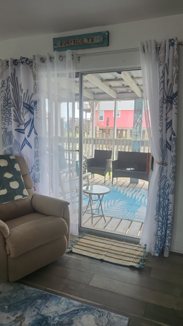 A room with a sofa, a small table, a sliding glass door leading to an outdoor patio with a pool, and a sign reading 'SURFSIDE TX'.