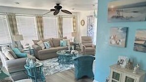 Sala de estar com sofá, cadeiras, mesa de centro, ventilador de teto e um armário com quadros.