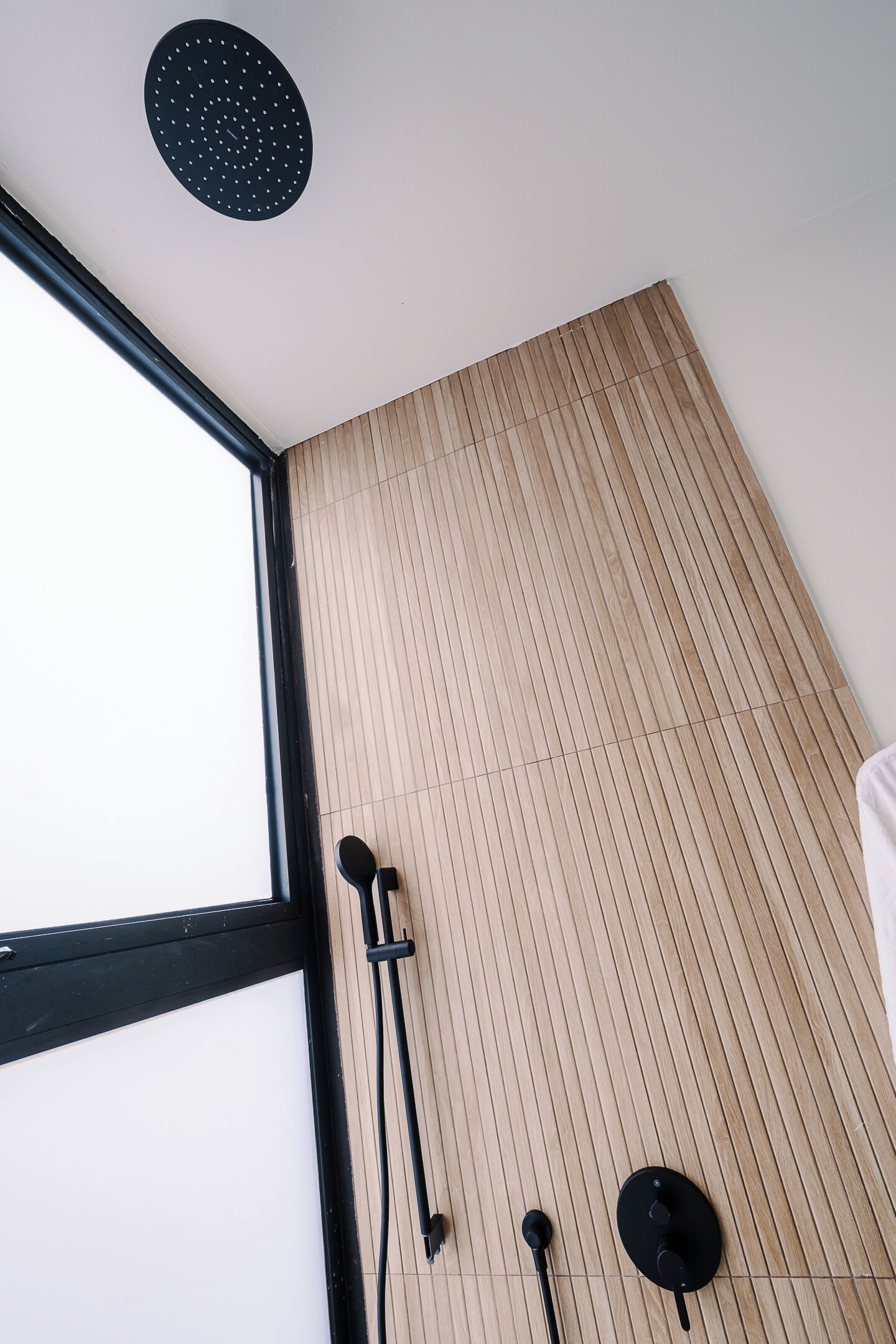 Una habitación con un ventanal grande, un muro de listones de madera y un plafón con una lámpara circular.