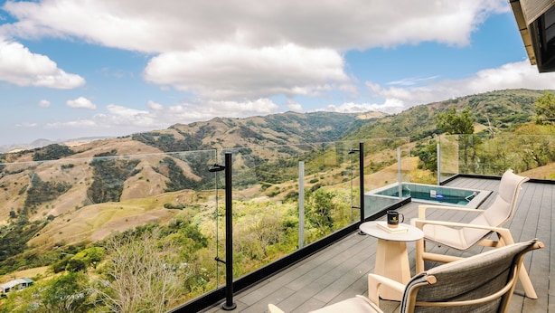 A deck with a glass-enclosed hot tub, outdoor seating, and a view of rolling hills. - Cozy 2-bedroom villa in serene Monteverde with Pool and AC (Monteverde)