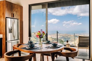 A dining area with a large window, a stainless steel refrigerator, and a table set for two.