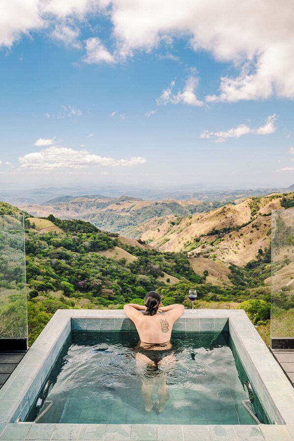 A person relaxing in a hot tub with a scenic view of hills and valleys.