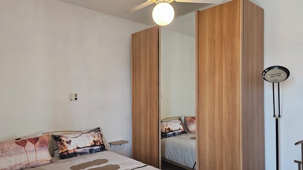 Une chambre à coucher avec un lit, une table de chevet, un miroir et un ventilateur de plafond.
