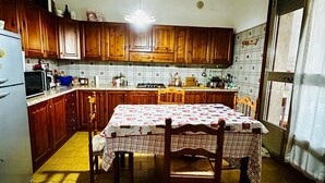 A kitchen with wooden cabinets, a dining table with a checkered tablecloth, a hanging light fixture, and a window with curtains. - Relaxation one step away from Gardaland spas and beaches.... (Lazise)