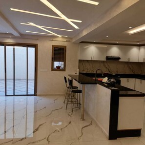 A modern kitchen with a marble countertop, a bar stool, and a large island. - Akenza Hospitality. Pleasant family stay in a superb villa with private pool (Marrakesh)