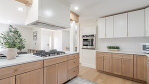 Une cuisine moderne avec des meubles blancs, un îlot central, des appareils en acier inoxydable et un plancher en bois.