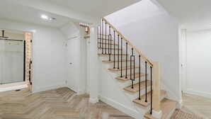 Un intérieur moderne avec un escalier en bois, une douche en verre et un parquet disposé en chevrons.
