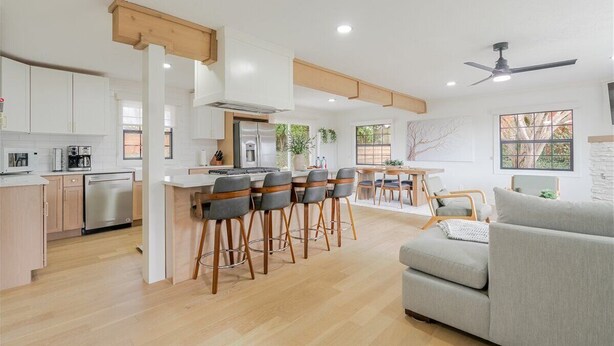 Une cuisine moderne dotée d’un îlot central, de tabourets de bar, d’un coin repas avec une table et des chaises, et d’un salon avec un canapé.