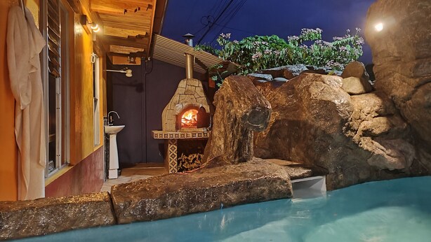 Ein Kamin aus Stein mit Feuer, ein Pool und eine Holzbalkendecke.