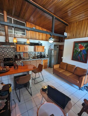 Eine Küche mit Holzausstattung, ein Essbereich mit Tisch und Stühlen, ein Sofa und ein Fernseher.