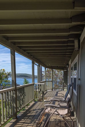 A covered porch with a view of the water, wooden railings, and a bench.
