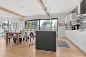 Una cocina moderna con armarios blancos, una isla central y una zona de comedor con mesa y sillas de madera.