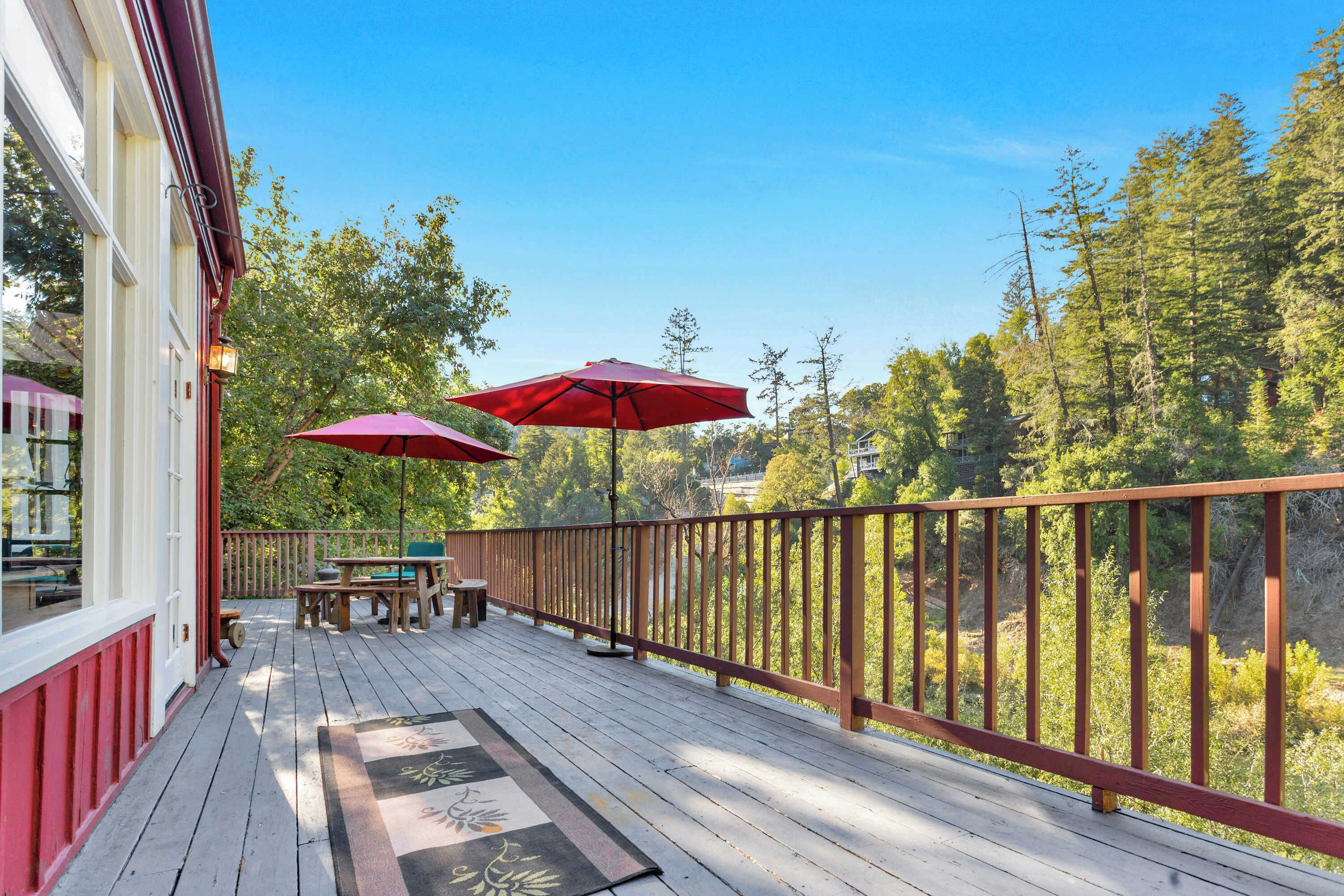 Une terrasse en bois avec une rambarde, des meubles d’extérieur et des parasols rouges.