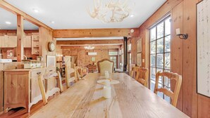 Un interior de madera con una larga mesa de comedor, sillas, un candelabro y un ventanal amplio.