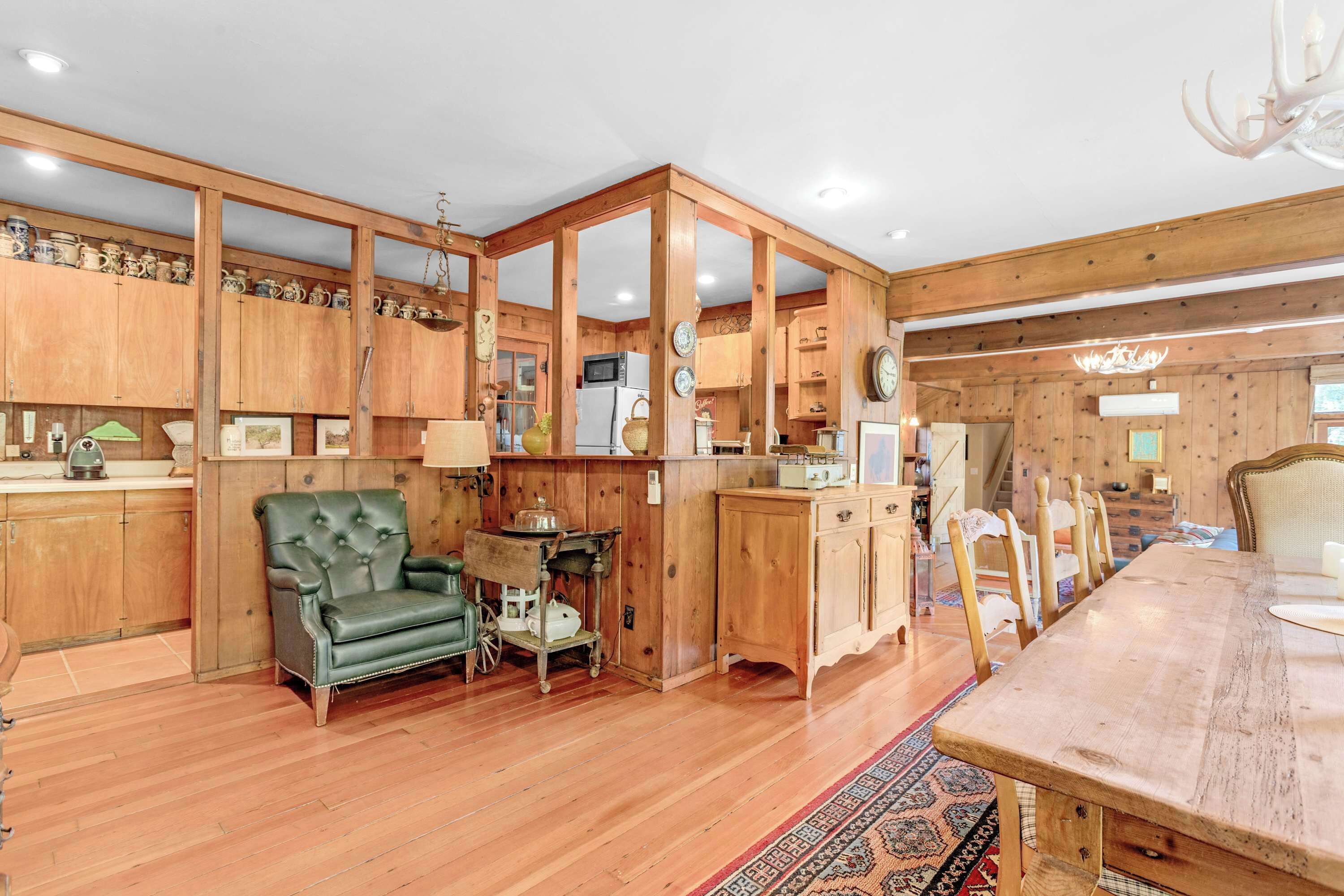 Un intérieur en bois comprenant une table à manger, des chaises, un fauteuil vert et un coin cuisine avec des placards et des appareils électroménagers.