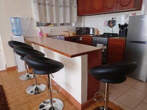 A kitchen with a central island, bar stools, a refrigerator, a stove, and a microwave.