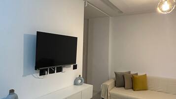 Una sala de estar moderna con un televisor de pantalla plana en la pared, un sofá con cojines, una mesa de centro y una lámpara decorativa.