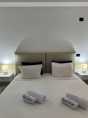 A double bed with two pillows, a headboard, two bedside tables with lamps, and two rolled towels with 'KeyndGo' branding. - Exceptional Apartment Luxury and Absolute Comfort (Tunis)