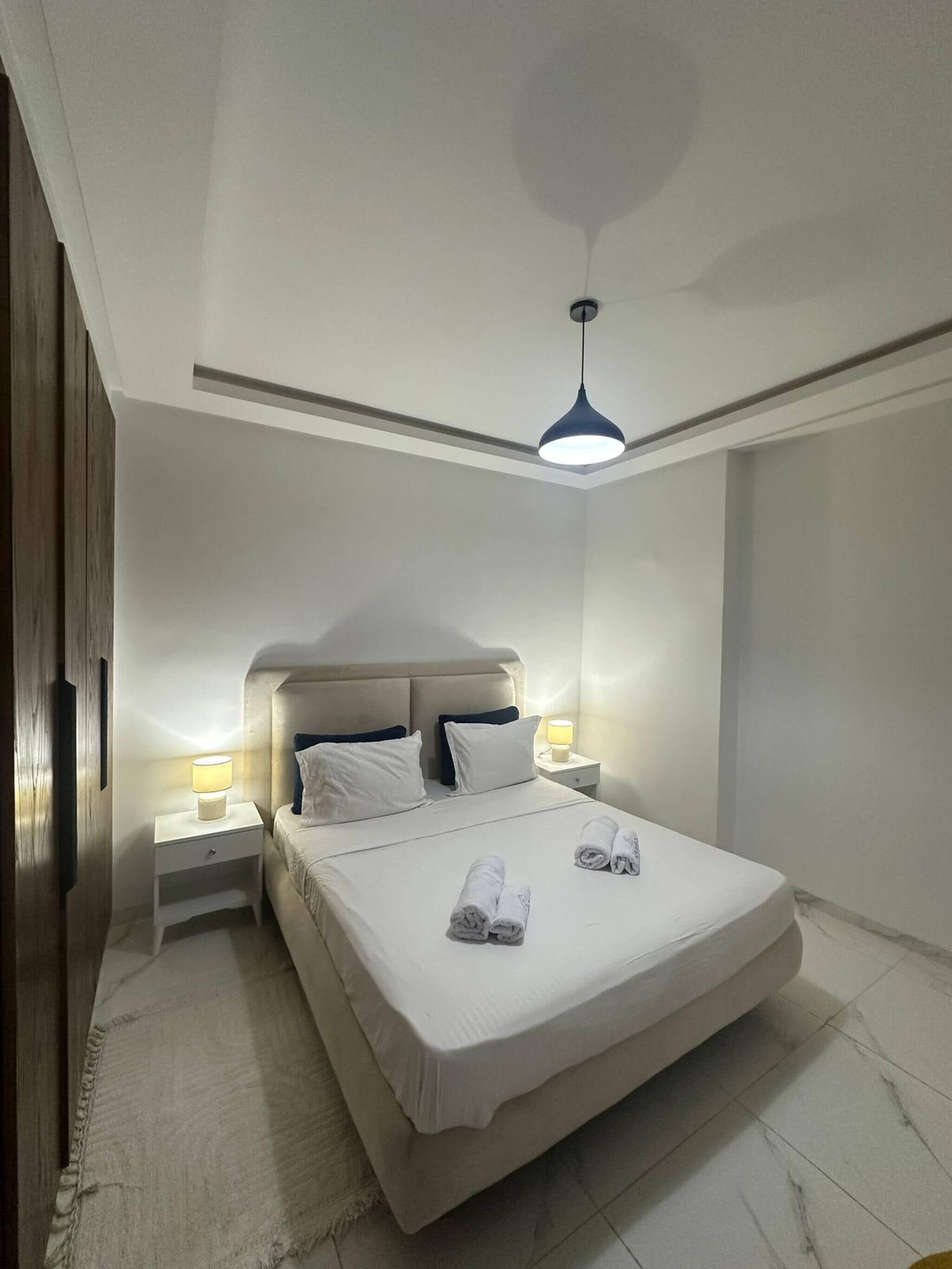 A neatly made bed with pillows and towels, a bedside lamp, and a ceiling light fixture.