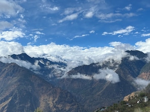 A mountainous landscape with snow-capped peaks, a clear sky, and a valley with scattered houses.