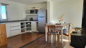 Eine moderne Küche mit weißen Schränken, einem Edelstahl-Kühlschrank und einem Essbereich mit einem Holztisch und gestreiften Stühlen.