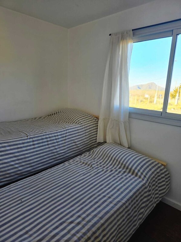 Une chambre individuelle avec deux lits, une fenêtre donnant sur un paysage et un rideau.