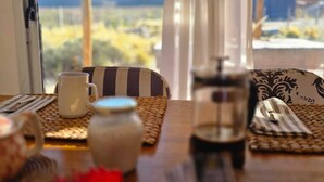 Ein Esstisch mit Kaffeemaschine, Tasse und Einmachglas, mit Blick auf eine gebirgige Landschaft durch ein Fenster.